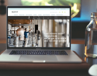 A laptop on a table displays a website with an image of a person in an industrial setting and text that reads, Last minute order? No problem—we’ve got it in stock and can ship quickly.